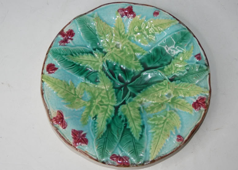 A decorative ceramic plate with green leaves and red flowers on a light blue background.