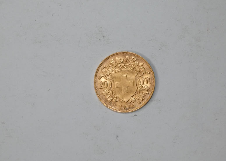 A gold coin with intricate designs and text, placed on a plain gray background.