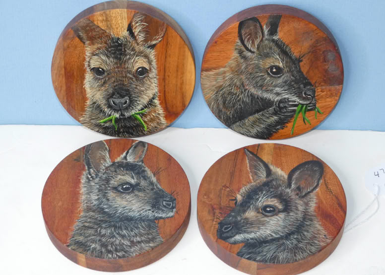 Four round wooden coasters featuring painted images of small animals resembling wallabies, each with a different pose.
