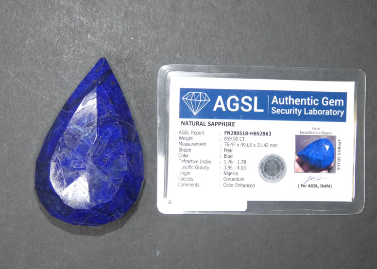 A pear-shaped blue gemstone next to a certification card labeled "AGSL Authentic Gem Security Laboratory" with details and a small image of the gemstone.