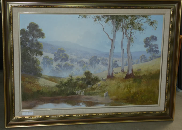 A framed landscape painting depicting rolling hills, trees, and a small body of water in the foreground.