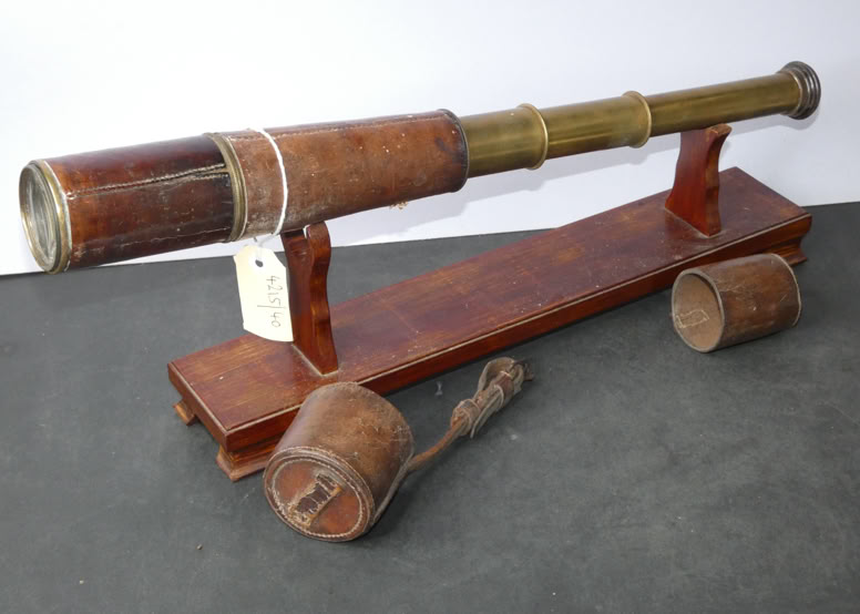 A vintage brass and leather telescope on a wooden stand, with a detached lens cap and a wooden handle nearby.